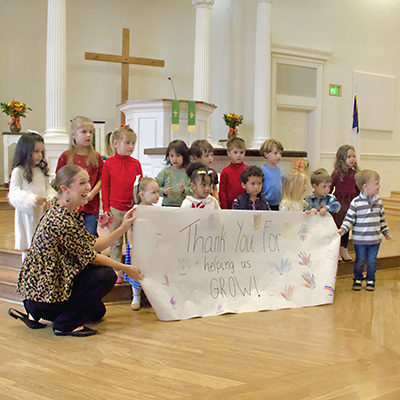 children hold a banner in front of the alter at Kernersville Moravian, thanking the congregation for helping them grow in Christ